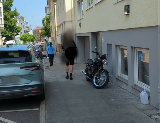Mitarbeiterin des Ordnungsamts läuft untätig an Motorrad und Auto auf Gehweg vorbei.