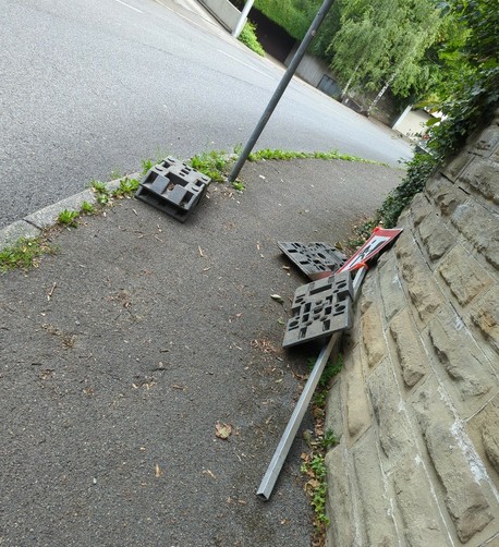 ein Baustellenschild liegt auf dem Gehweg, die Füße dazu überall verteilt