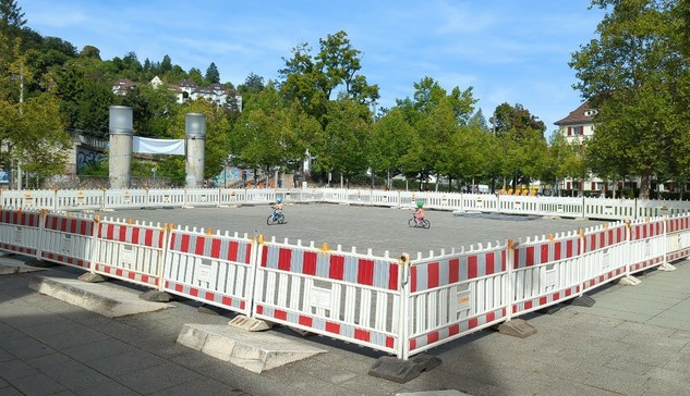 der Südheimer Platz ist mit Sperrbaken komplett eingezäunt. Zwei kleine Kinder fahren dort mit ihren Rädchen.